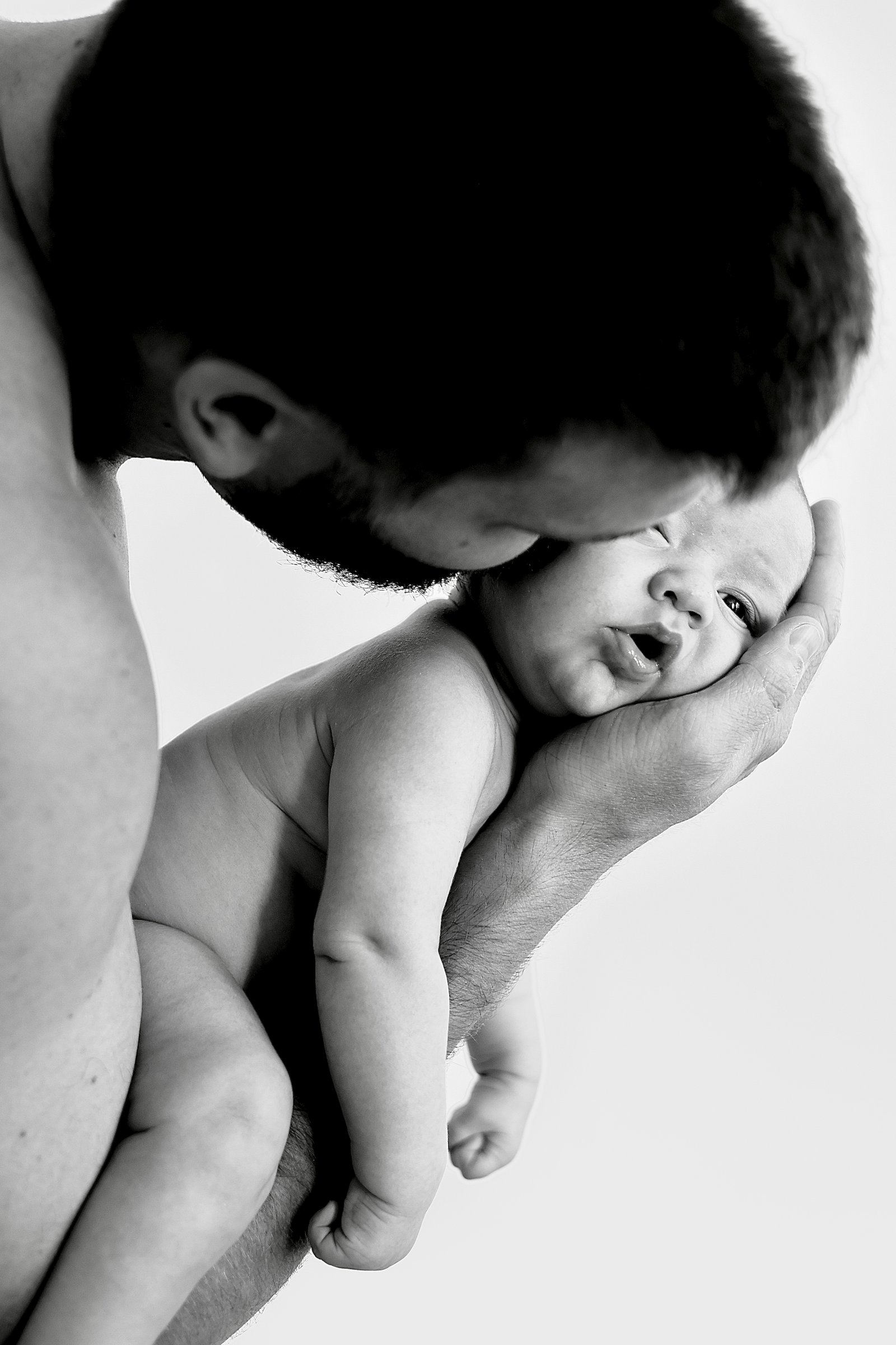 un nourrisson sur le bras de son papa qui l'embrasse 