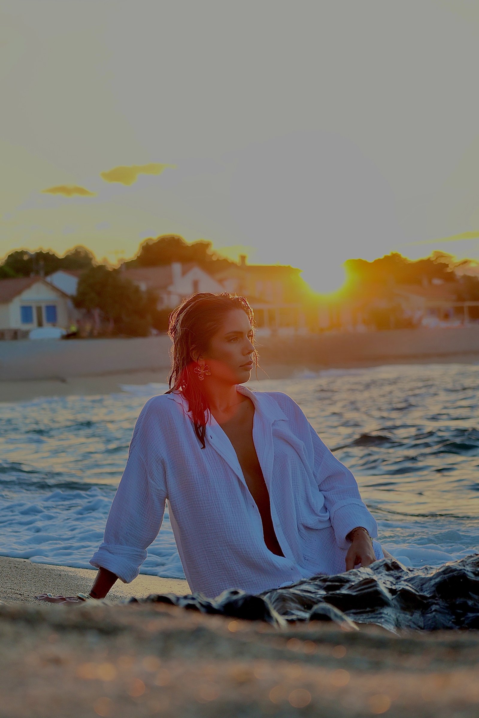 jeune femme assise au bord de l'eau avec le couché de soleil derrière elle 