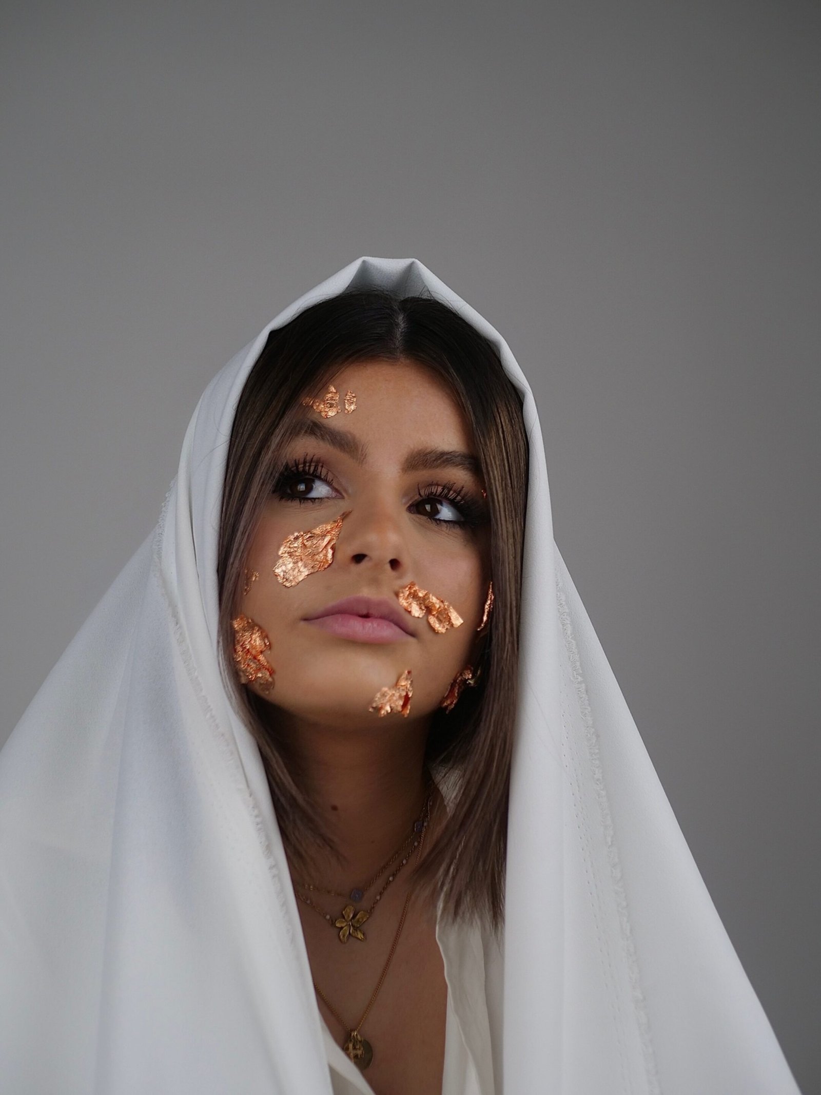 une jeune femme regardant voir le haut avec un drap blanc sur le cheveux et des feuilles d'or sur son visage