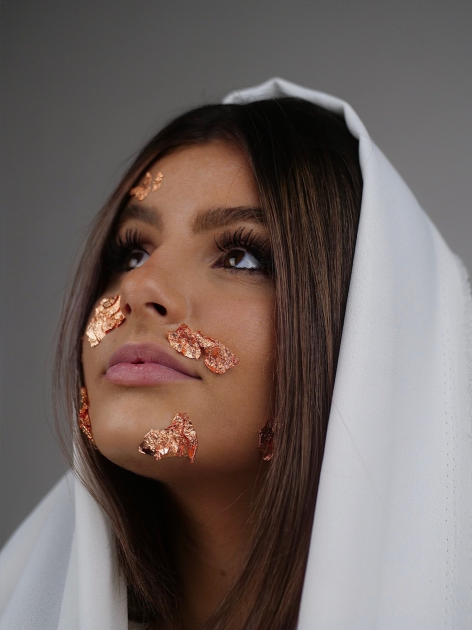 une jeune femme regardant voir le haut avec un drap blanc sur le cheveux et des feuilles d'or sur son visage 