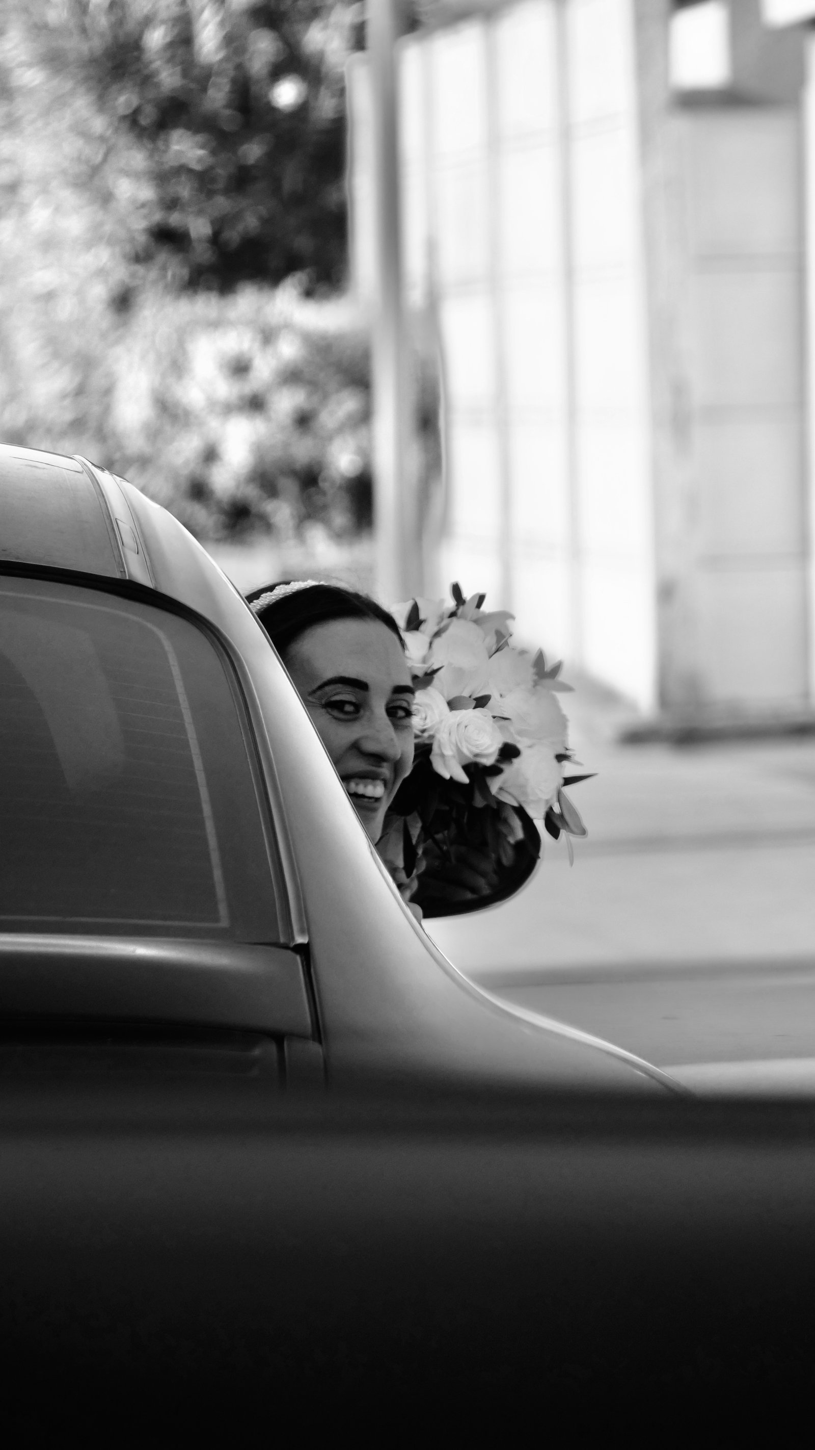 la mariée à la fenêtre de sa voiture le jour de son mariage avec son bouquet