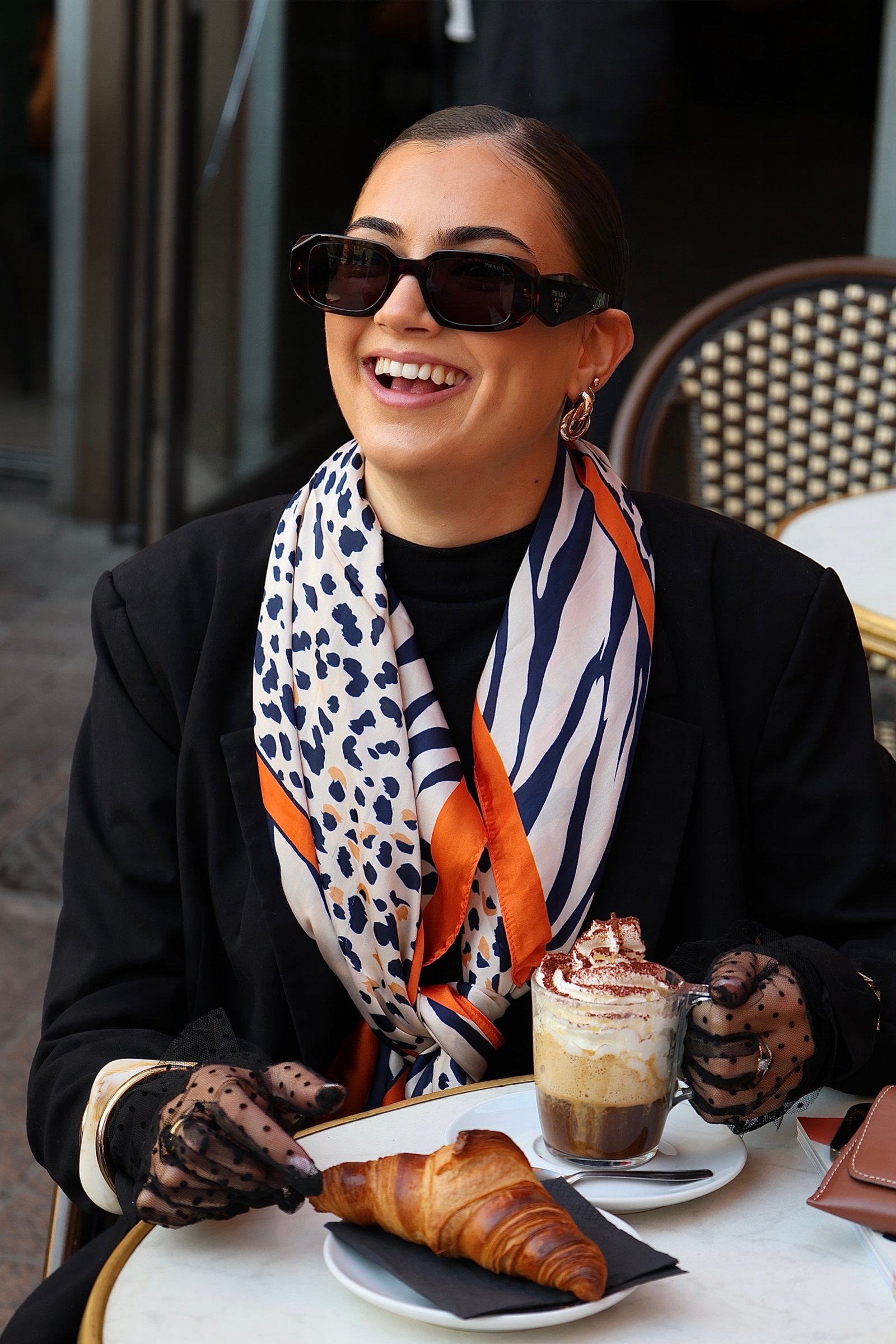 une femme qui souris avec son cafe a la main en terrasse 